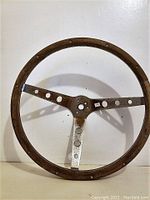 Front view of a 15-inch wooden Mustang steering wheel with a three-spoke metal center and circular cutouts in spokes.