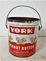 Front side of York peanut butter tin canister showing brand logo, peanut illustrations, product name in English, and condition with visible wear and rust.