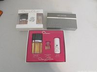 Three boxed gift sets on a gray table: two Oscar de la Renta sets and one Geoffrey Beene Grey Flannel gift box.