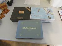 Three closed gift boxes including Tommy Bahama Very Cool, Beckham Intimately, Salvatore Ferragamo Acqua Essenziale arranged on a table.