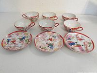Full set of 6 cups and 3 plates showing red painted rims and colorful hand-painted traditional Japanese style artwork.