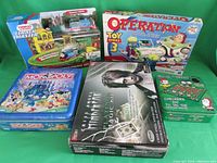 All five items displayed against green background showing sealed tins and boxed games and playset.