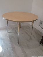 Jonti-Craft commercial round table with a maple laminated top and four steel legs shown in a room with wood floor.