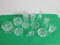 Full view of 12 pieces including ashtrays, jars, glasses, and candy dish arranged on green background.