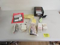 Overview of laminator with accessories and supplies spread out on table, including instruction manual, pouches, and small bags