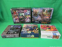 Front view of all puzzle boxes arranged on green background showing the puzzle titles and piece counts.