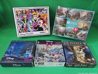 Front view of all five puzzle boxes showing Disney Villains 1500 pcs, Thomas Kinkade box containing 8 puzzles, Disney Thomas Kinkade Cinderella, Disney Thomas Kinkade Beauty and the Beast, Harry Potter Hogwarts Great Hall.