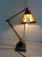 Full view of stained glass adjustable desk lamp lit, showing metal arm and decorative metal base. Ruler in background showing height up to 30 inches.