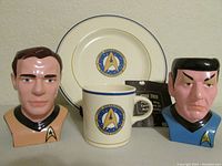 Front view of the Spock and Captain Kirk figurine mugs with the USS Enterprise plate and matching mug, and certificate of authenticity visible between.