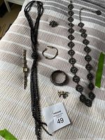 Overview of assorted costume jewellery laid on bed including necklaces, bracelets, brooch, pin and watch with lot tag