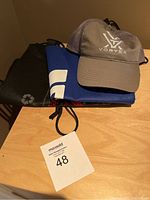 Gray Vortex baseball cap on top of folded bags on a wooden surface with auction lot number 48 card.