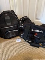 Both bags placed on carpet; left is a black Lowepro camera bag with visible front pockets; right is a black Reebok hockey bag with handles and logo visible.