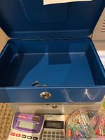 Blue metal cash box open showing empty interior and keys inside