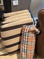 Four brown and tan striped chair cushions stacked beside a folded plaid picnic blanket showing pattern details and tied straps on cushions.