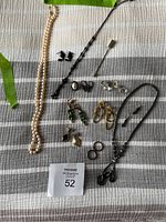 Overview of assorted costume jewellery including necklaces, earrings, rings, and brooches arranged on striped fabric.