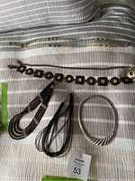 Six assorted pieces of costume jewelry including chains, bead necklaces, and a bracelet on a striped fabric background.