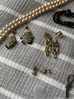 Close-up of various earrings and two necklaces, showing styles and condition.