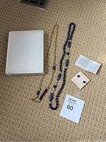 Full set of lapis lazuli jewelry including two necklaces, earrings, an information card, and a jewelry box on carpet.