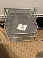 Metal mesh desk paper stand with two trays sitting on carpet.