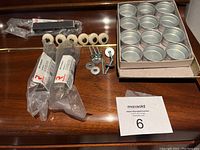 Overview of the lot: plastic-wrapped Richelieu drawer pulls, vintage round knobs, metal washers, screws, and dozen mini storage tins in a cardboard tray