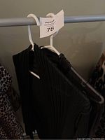 Black knit ribbed cover-up sweater on hanger shown folded on clothing rack.