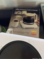 Saltin hot plate with black heating surface, white base, and glass coffee pot shown with original box in background.