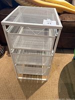 White IKEA mesh cart displaying four pull-out drawers on a carpeted floor in front of a couch.
