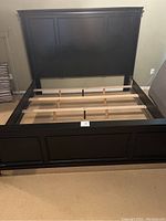 Black king bed frame showing headboard, footboard, side rails with additional wooden support slats and legs for mattress support.