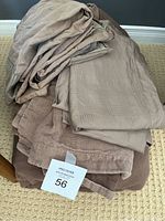 Stack of folded corduroy bedding items including duvet cover, shams, and pillowcases in muted taupe and brown shades laying on a beige carpet.
