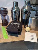 Photo of entire lot showing two martini shakers, Kuraidori wine aerator, PlayStation stainless steel flask, gear shift knob wine bottle stopper, two black beer coozies, and a green packing tape
