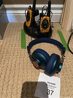 Two Motorola walkie talkies placed in a black dual charging station and a pair of blue Marley headphones on a beige carpet.