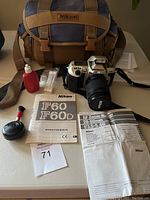 Nikon F60 camera with 28-80mm lens, carrying case, cleaning kit and instruction manuals on table.
