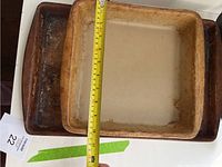Square stone brownie baking pan with tape measure across to show width, sitting on top of a rectangular darker baking stone.