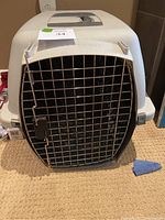 Front exterior view of plastic pet crate with metal wire door and latch, labeled with lot sticker.