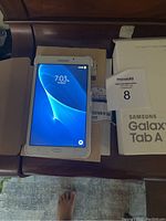 Samsung Galaxy Tab A6 powered on, with charging cable and original box shown.