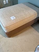 Full view of microfiber ottoman showing the rectangular beige cushion top and light brown base with wooden legs.