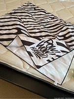Photo of zebra striped beach towel folded on mattress showing design and text
