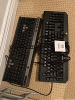 Two black mechanical keyboards side by side on carpet, with cables partly tangled. One keyboard is Razer, the other Corsair.