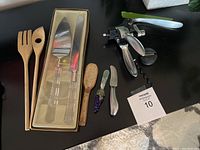 Photo showing two wooden salad tossers, the cake server set in packaging with clear handles, two cheese spreaders with decorative handles and a rabbit-shaped metal wine opener.