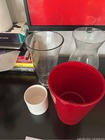 Four vases arranged on a black surface in front of a monitor and books, showing size and shape differences.