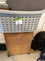 Plastic laundry basket sitting on top of a wicker laundry basket. Wicker basket has a woven pattern and fabric lining inside. Plastic basket is grey with a lattice pattern and has a visible crack on the side.
