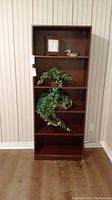 Front view of tall, dark brown manufactured wood bookcase with five shelves, empty except some decorative items removed (not included in sale).