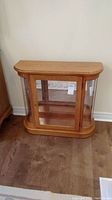 Front view of oak and glass display cabinet showing curved glass sides, glass shelf inside, and oak frame.