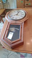 Side angled view of the full clock showing octagonal wood frame, glass front with 'REGULATOR' lettering and emblem, on a wooden table.
