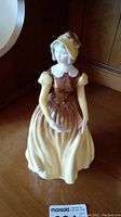 Front view of the Coalport figurine of a lady in bonnet and dress holding a letter.