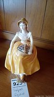 Front view of Lady of Fashion Constance Coalport porcelain figurine, showing detailed face, yellow dress, and basket of fruit on lap.