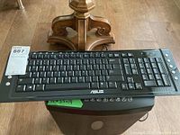 Full view of Asus black wired keyboard placed on top of a black paper shredder, showing the overall condition and setup.