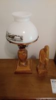 Full view of wood table lamp with white scenic glass shade and signed carved wood figure on wood surface