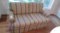 Front view of the striped upholstered love seat showing two cushions and rolled arms.