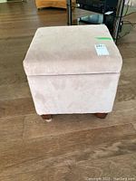 Front view of beige ultrasuede square storage ottoman on wooden floor, showing overall shape and fabric texture.
